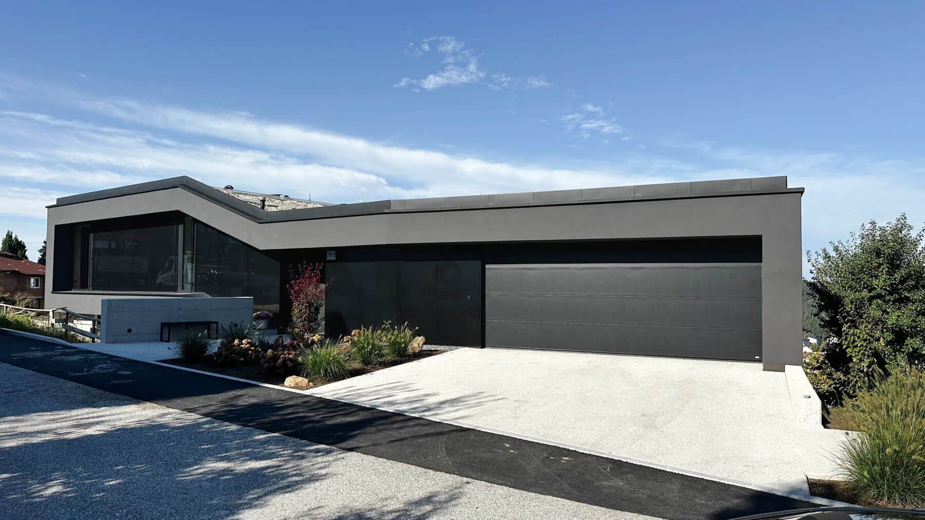 Modernes Einfamilienhaus mit dunkler Fassade und Flachdach vor blauem Himmel