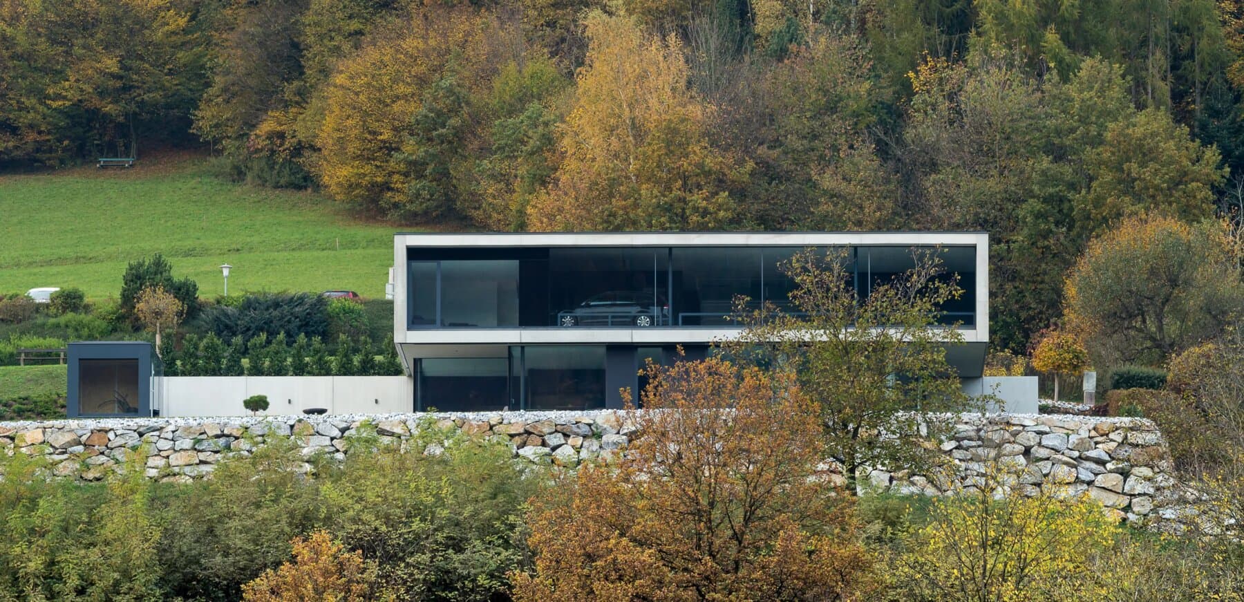 Flache Villa mit Glasfront und Steinmauer am Hang